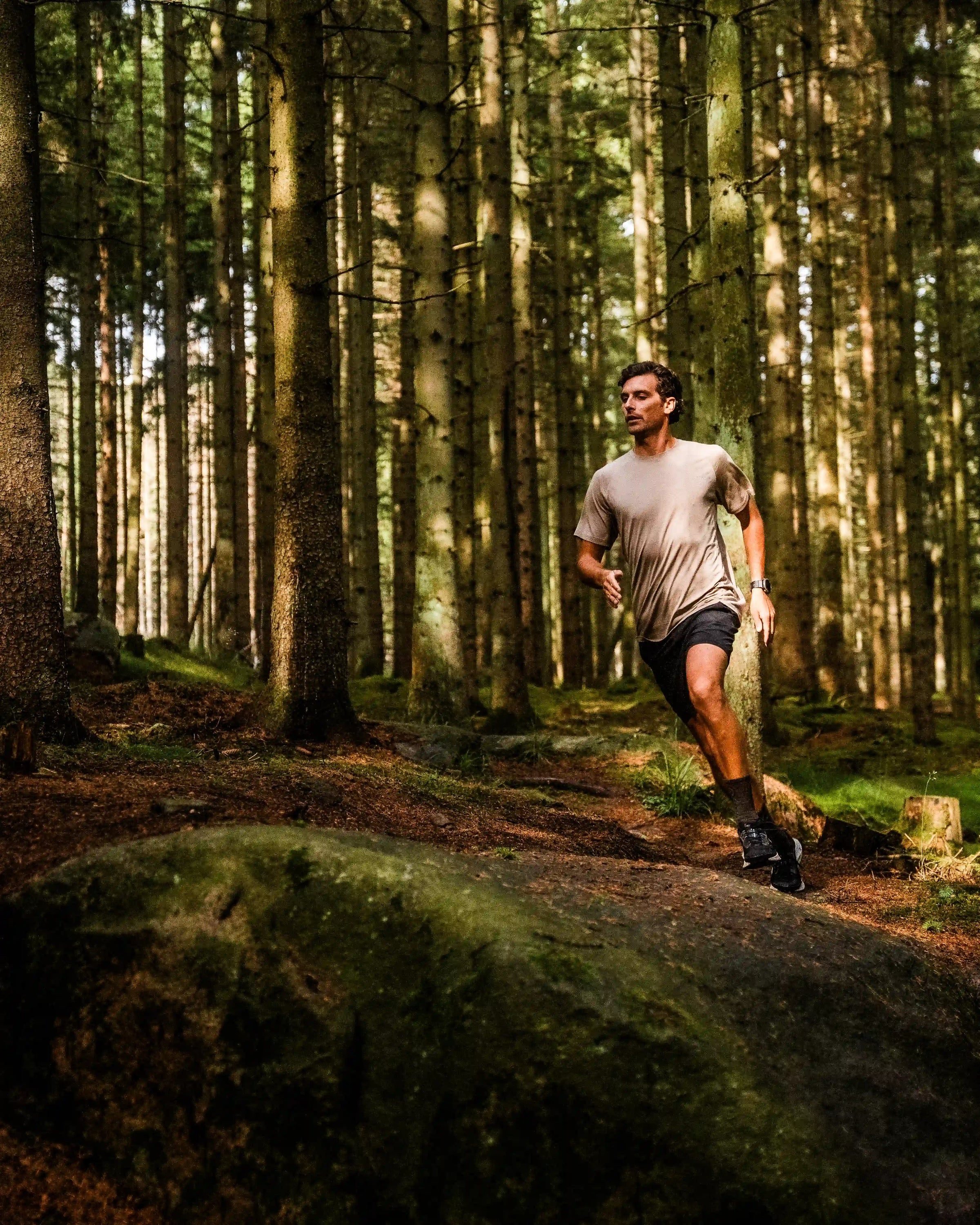Man løber gennem skoven i en sand-farvet t-shirt